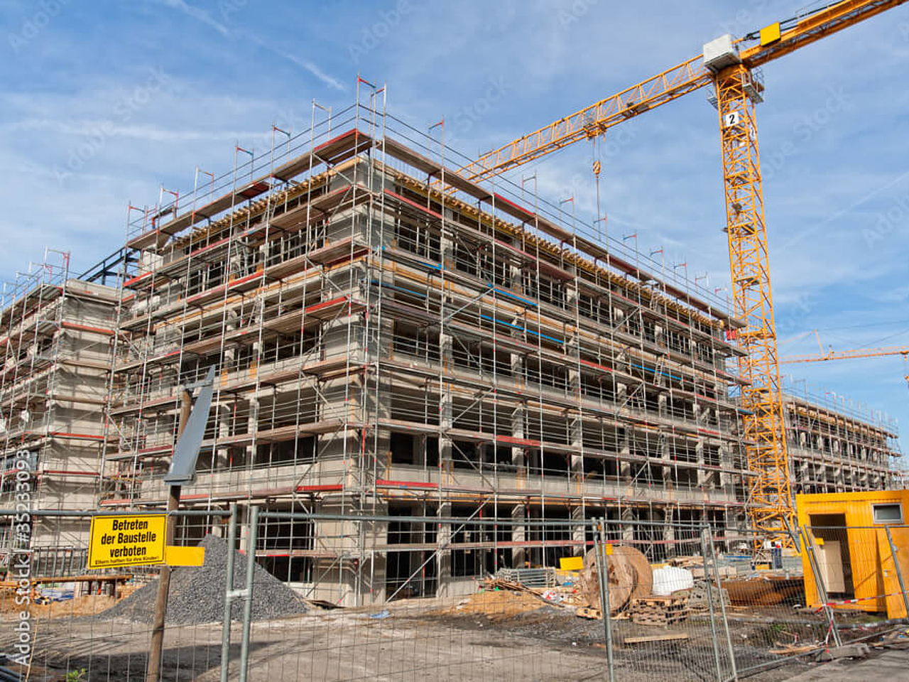 Mehrstöckiges Gebäude im Rohbau mit Baugerüst und mehreren Kränen auf einer weitläufigen Baustelle.