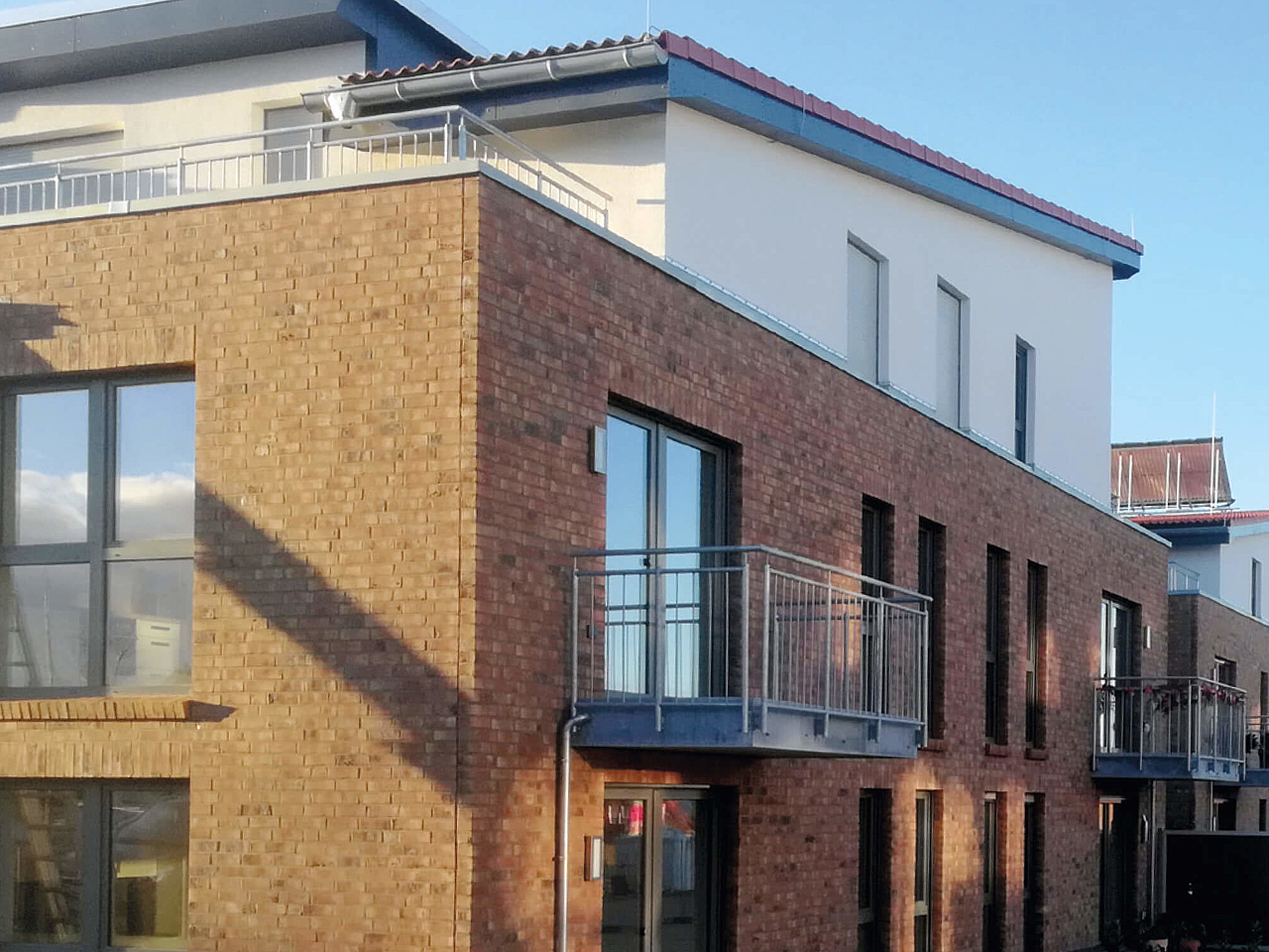 Modernes mehrstöckiges Wohngebäude mit Backsteinfassade, großen Fenstern und Balkonen.