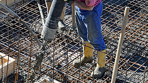 Bauarbeiter füllt flüssigen Beton mit einem Schlauch in eine Stahlbewehrung.